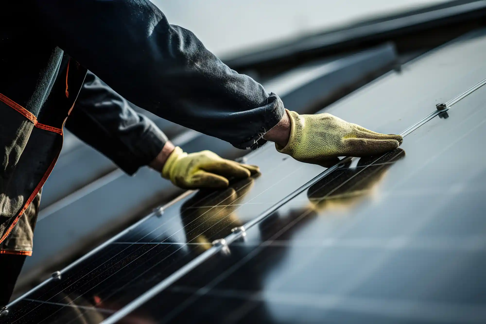 A person wearing yellow gloves is inspecting a row of reflective solar panels, likely involved in a commercial solar installation. 