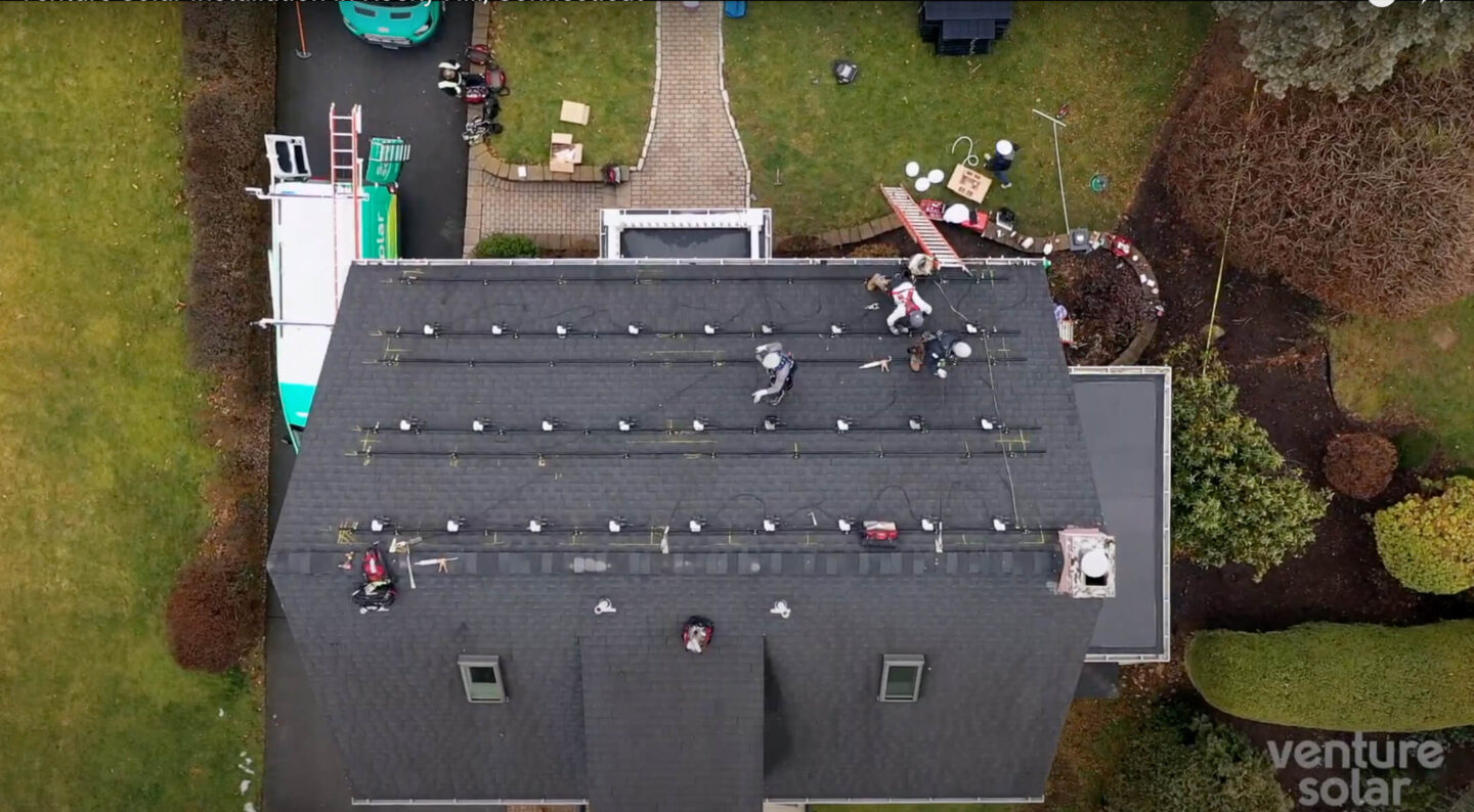 Aerial view of Venture Home workers diligently installing solar panels on a residential roof.