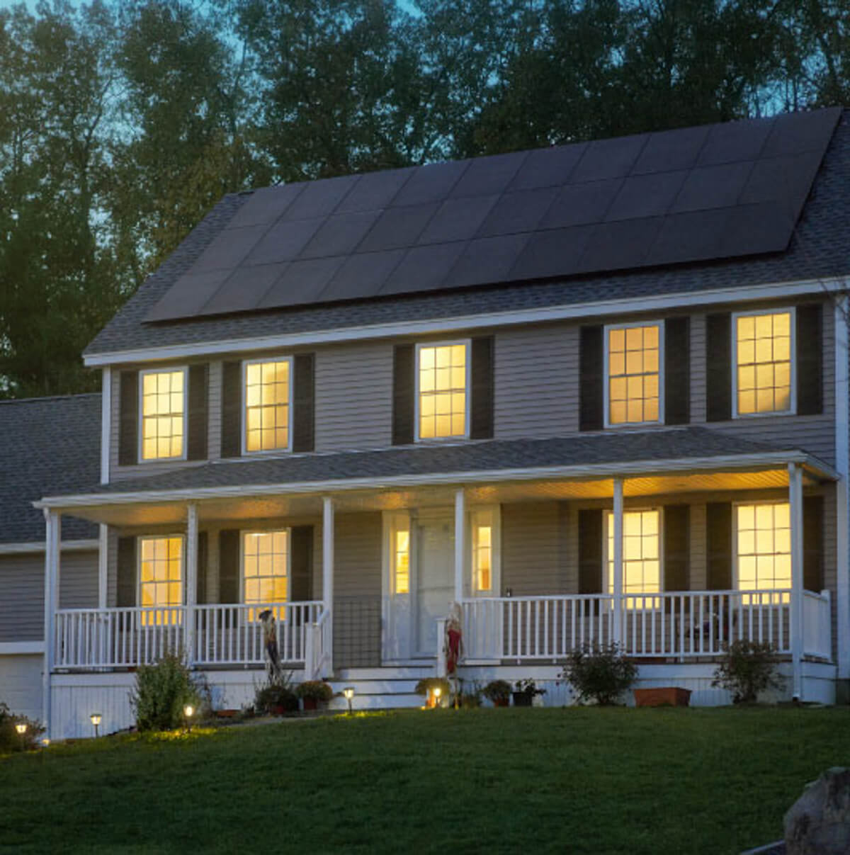 A house at night with solar panels on the roof, illuminated by light shining through the windows.