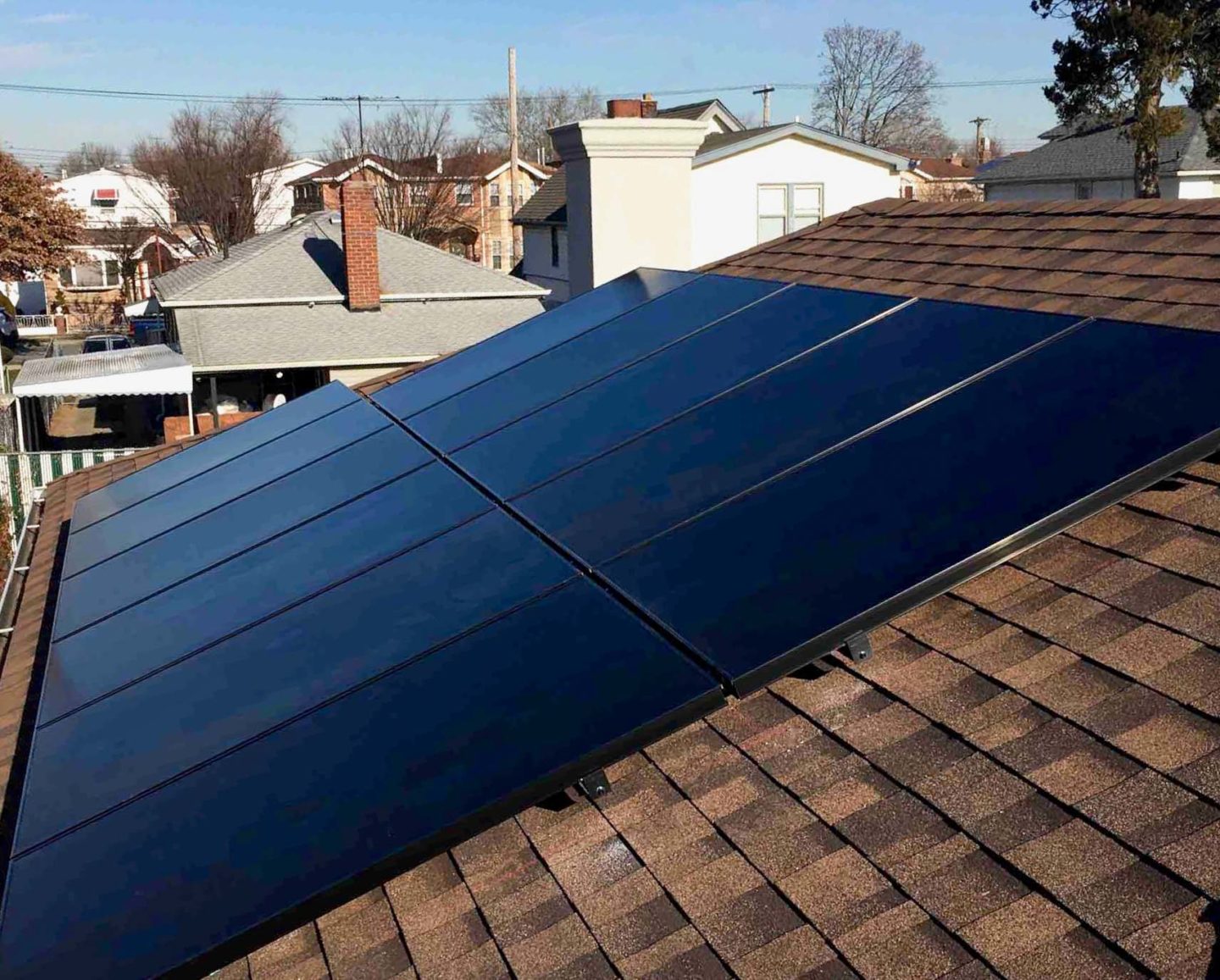 A close-up view of solar panels installed on a roof, with surrounding homes and clear blue skies in the background.