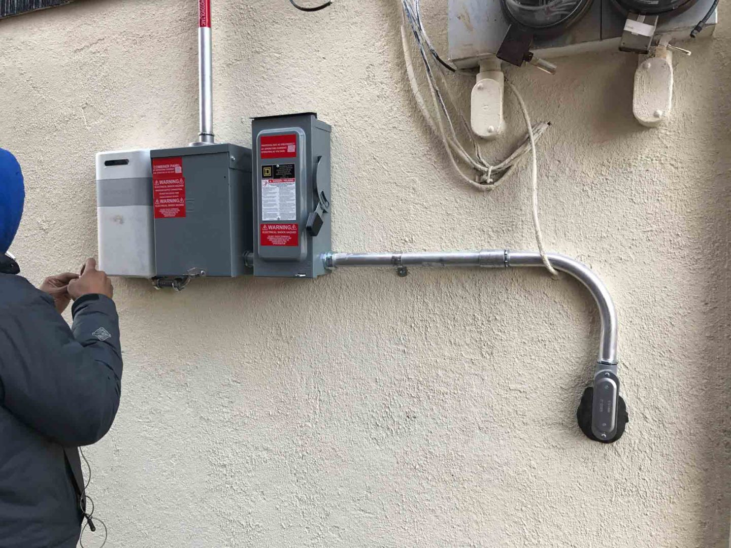 The side of a house with solar equipment, featuring a solar inverter, meter, and disconnect box.