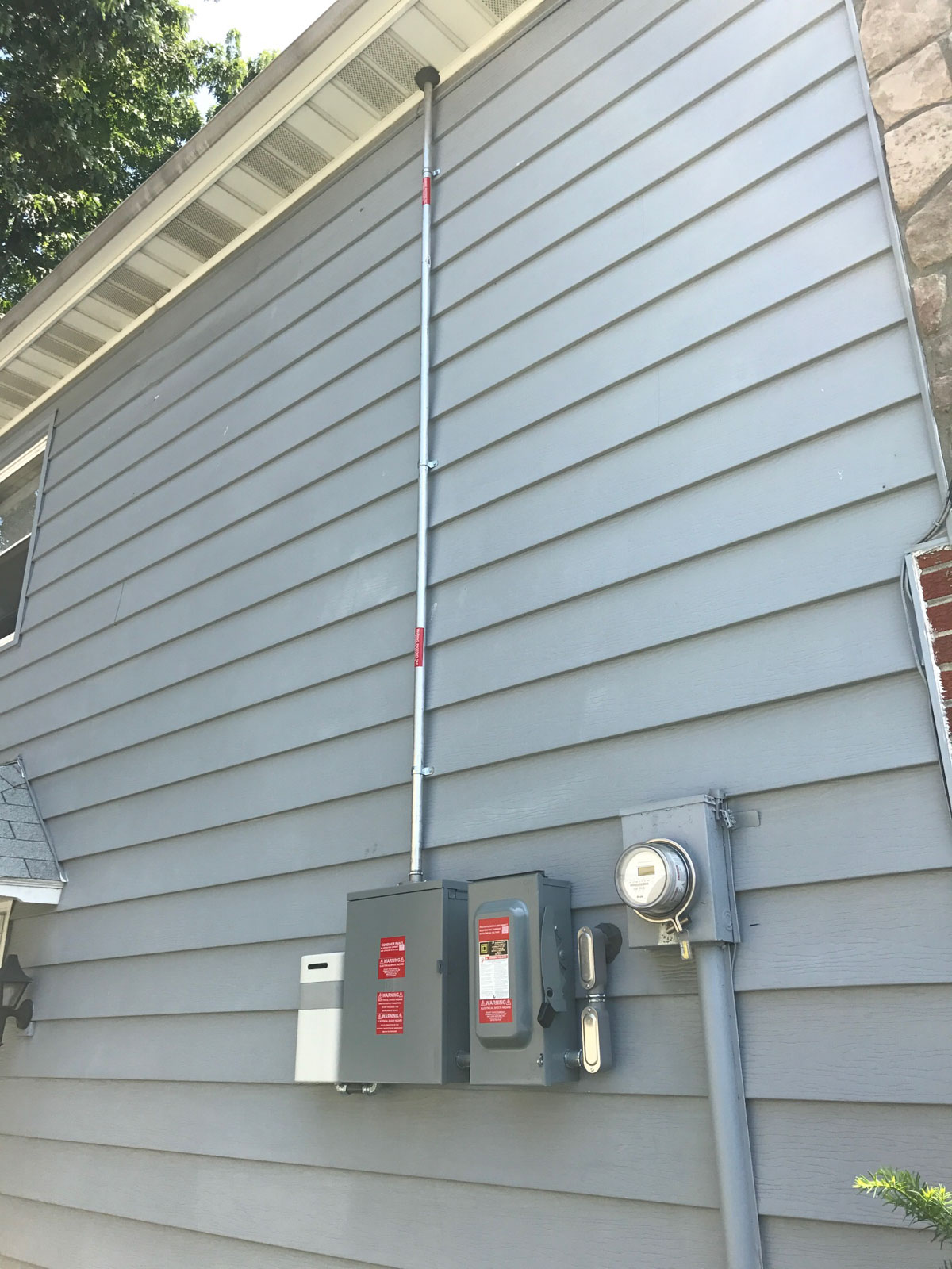Solar equipment mounted on the side of a house, featuring a solar inverter, meter, and electrical disconnect box.