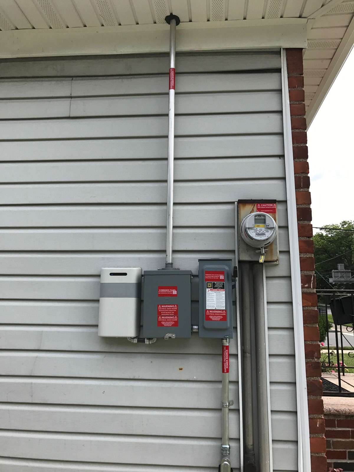 Solar equipment on the side of a house, including a solar inverter, meter, and electrical disconnect box.