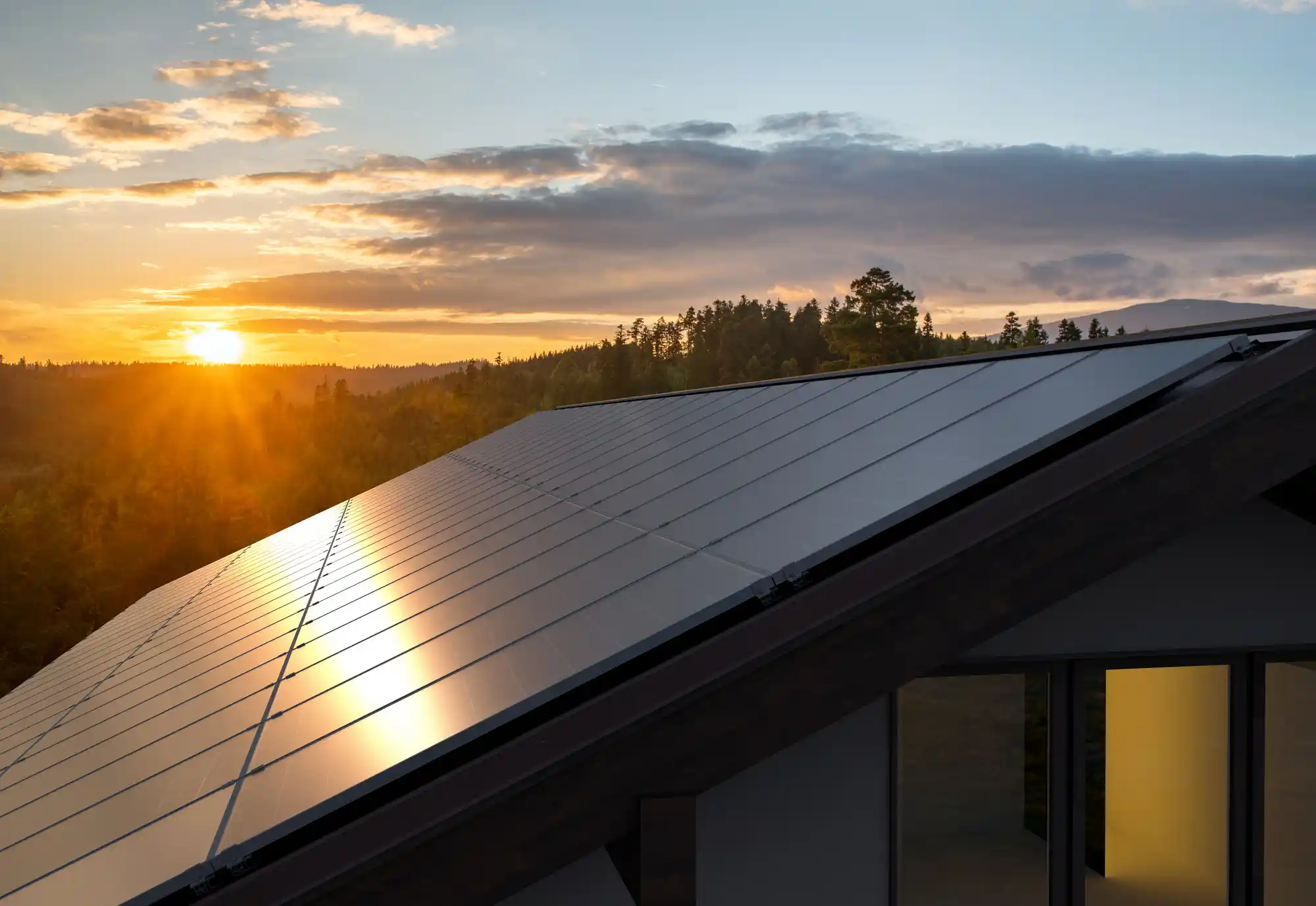 A rooftop adorned with glistening solar panels is showcased at sunset, the suns warm glow enhancing their sleek design.