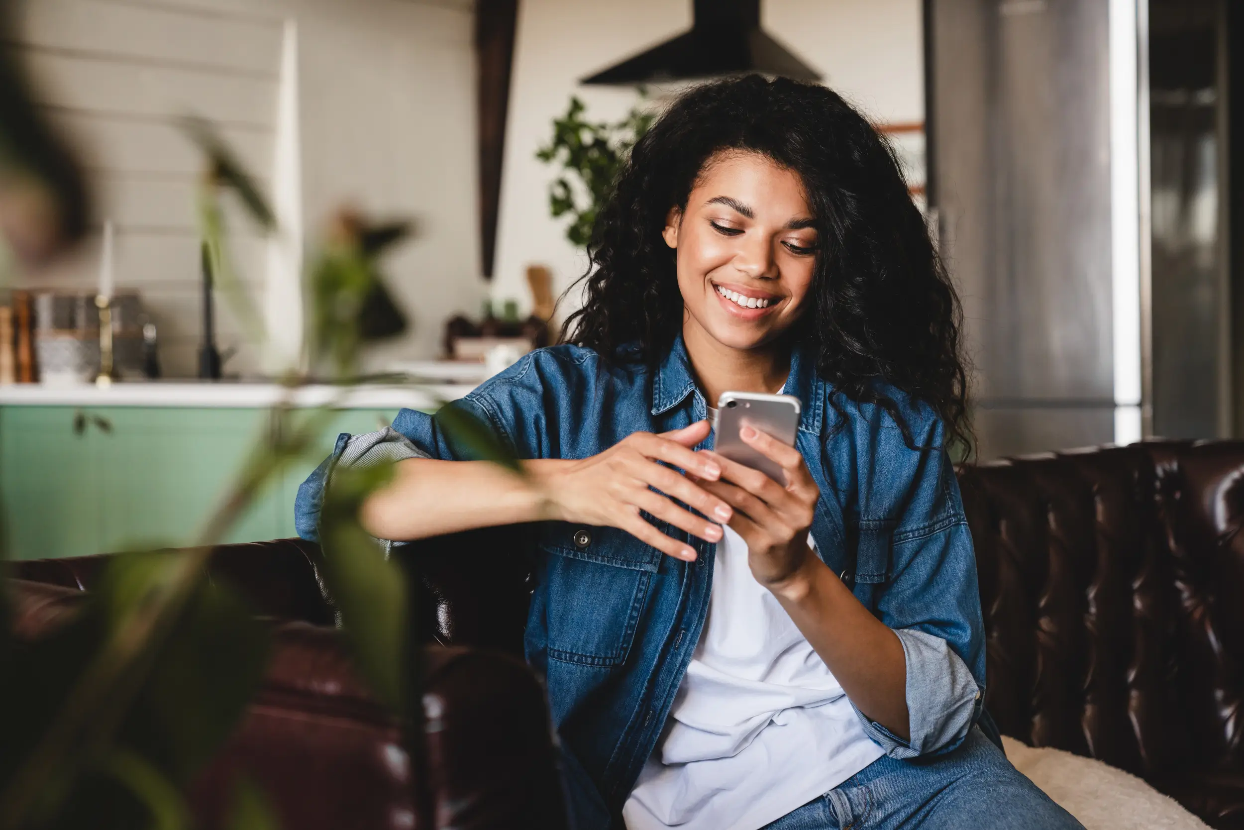 A woman sits on a couch, smiling at her smartphone in a modern, cozy living room filled with natural light from nearby solar panels.