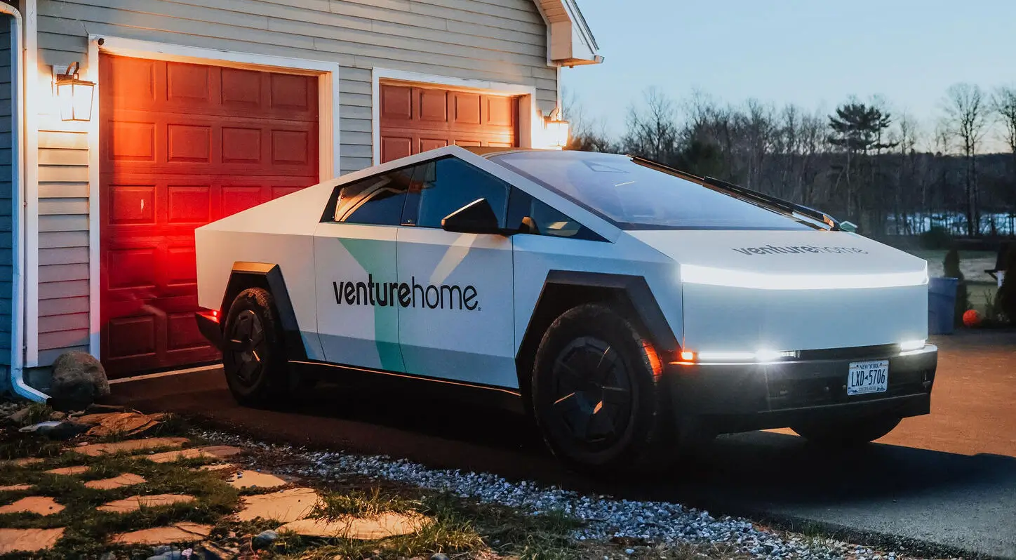 A futuristic pickup truck with venturehome. branding, parked beside a house with red garage doors and rooftop solar panels at dusk.
